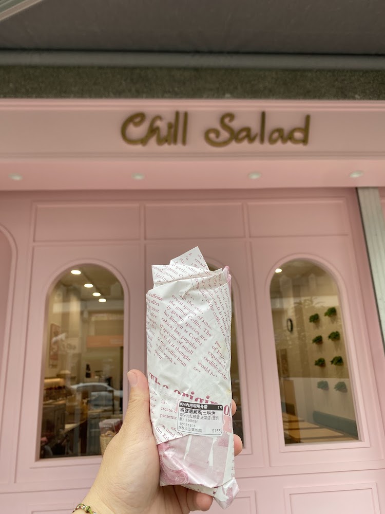 這張圖片主要內容是一隻手拿著包裝好的捲餅，背景是一家名為Chill Salad的粉紅色店面，看起來非常有設計感。