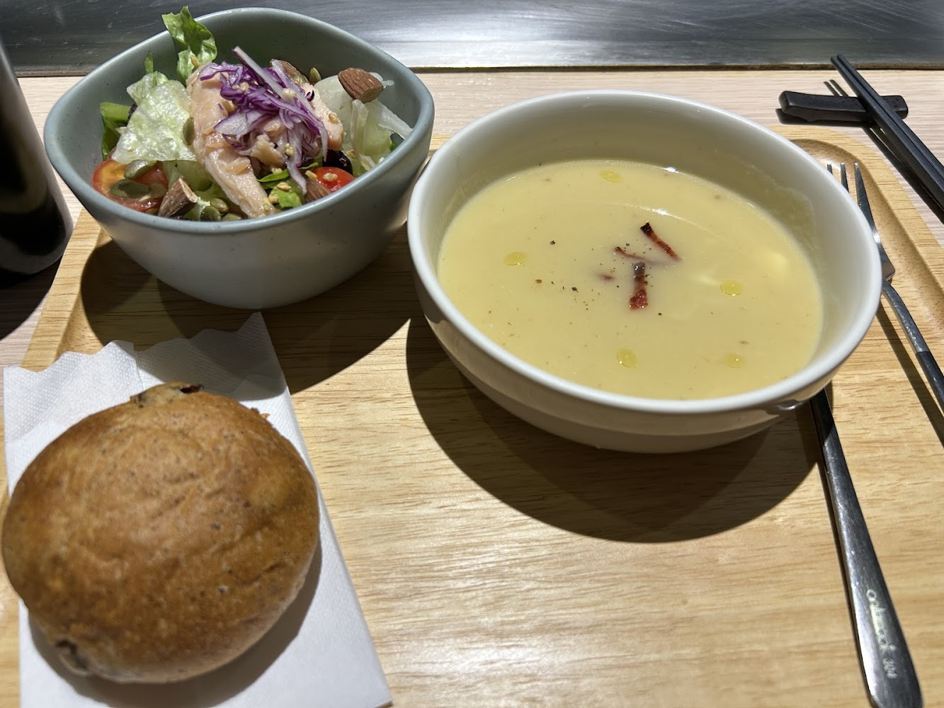 這張圖片主要有一碗濃湯、一碗生菜沙拉和一個全麥麵包。沙拉裡有鮮蔬、堅果與雞肉，餐具整齊擺放在托盤旁，整體營養均衡、健康美味。