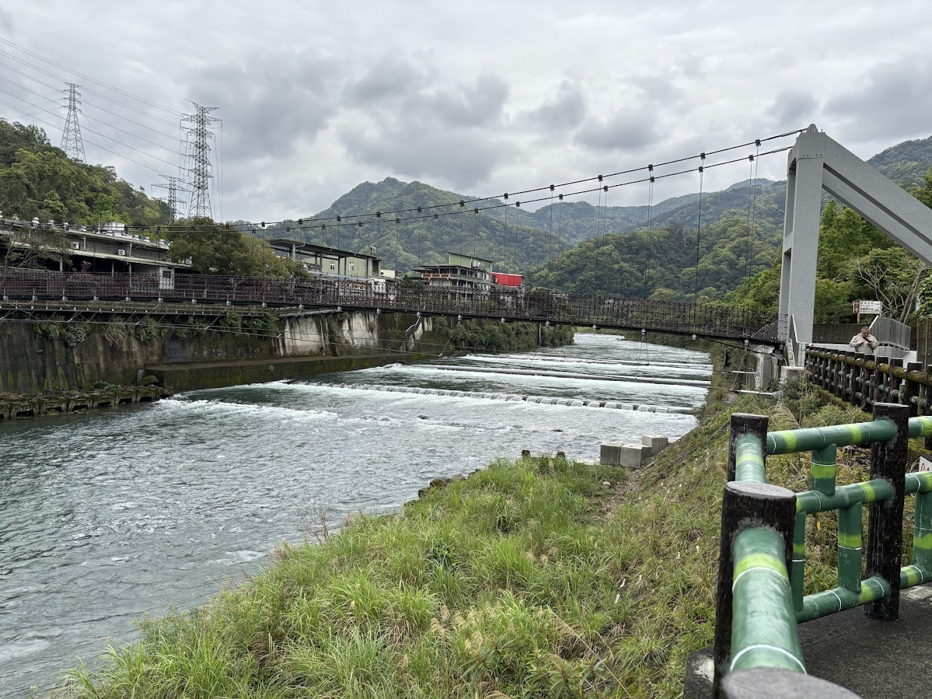 寬闊河流與吊橋、山景及建築構成的觀魚步道入口景觀
