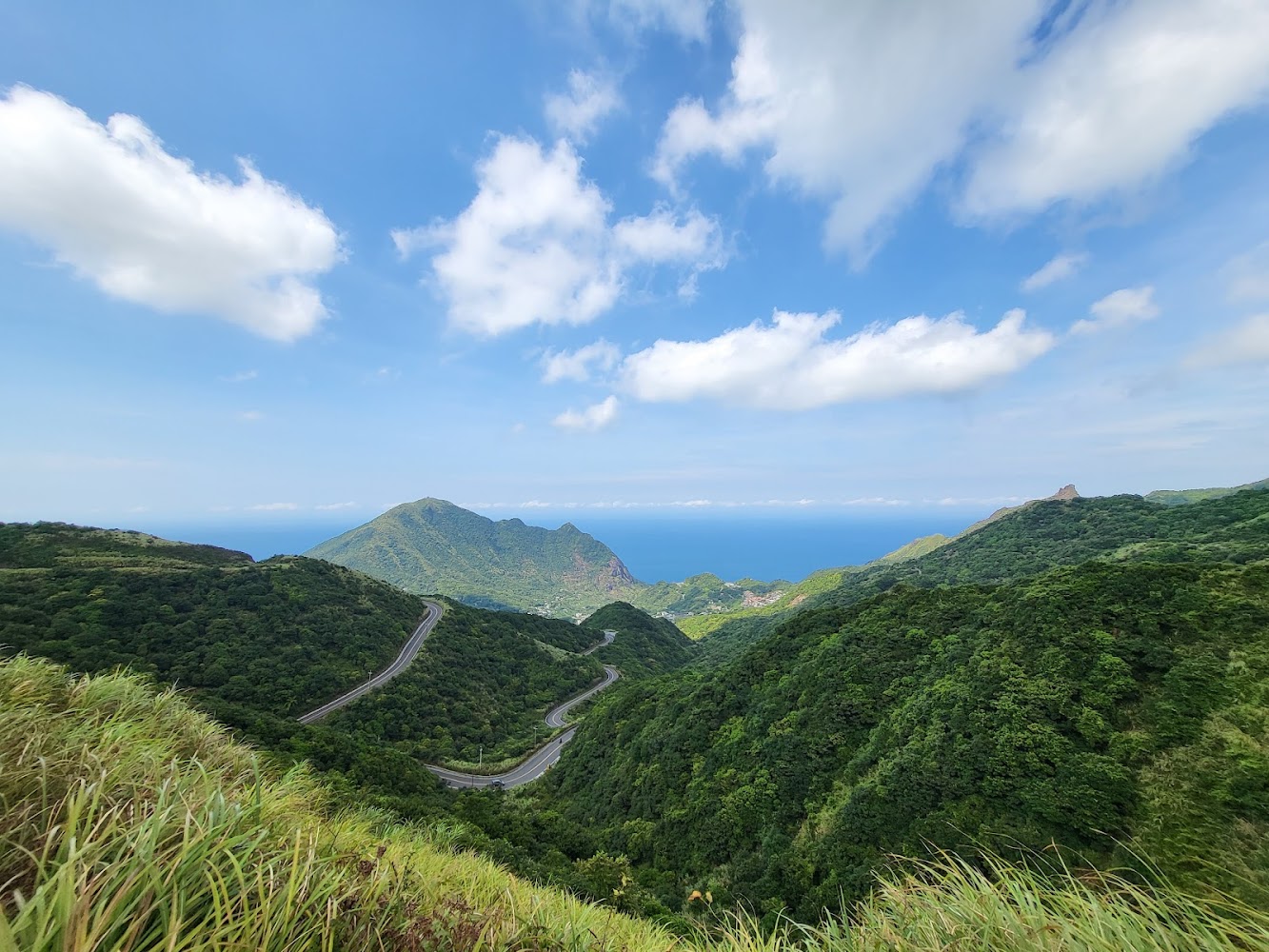 綠色山巒起伏遠方可見大海與藍天白雲