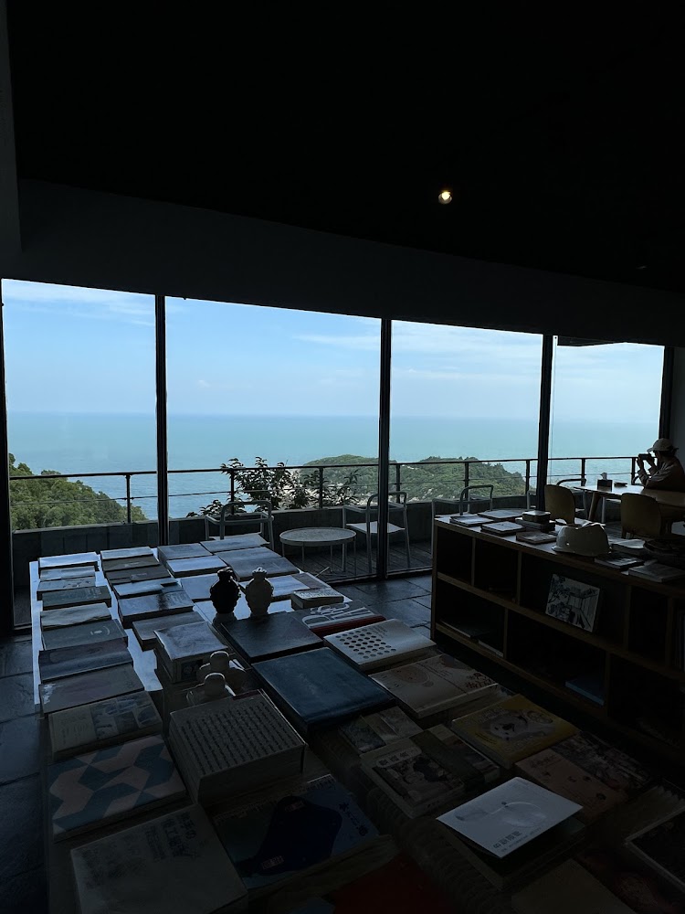 有大片落地窗的書店或咖啡廳，窗外可見藍色海景和綠色山丘