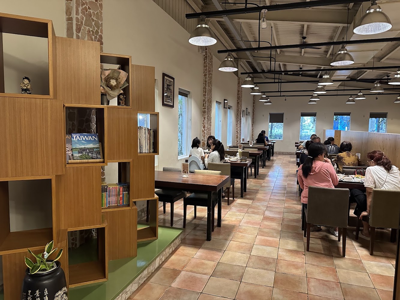 這張圖片主要呈現一家裝潢溫馨的餐廳，內有木質書架、書籍及擺飾，客人在桌邊用餐聊天，環境明亮寬敞，氣氛舒適悠閒。