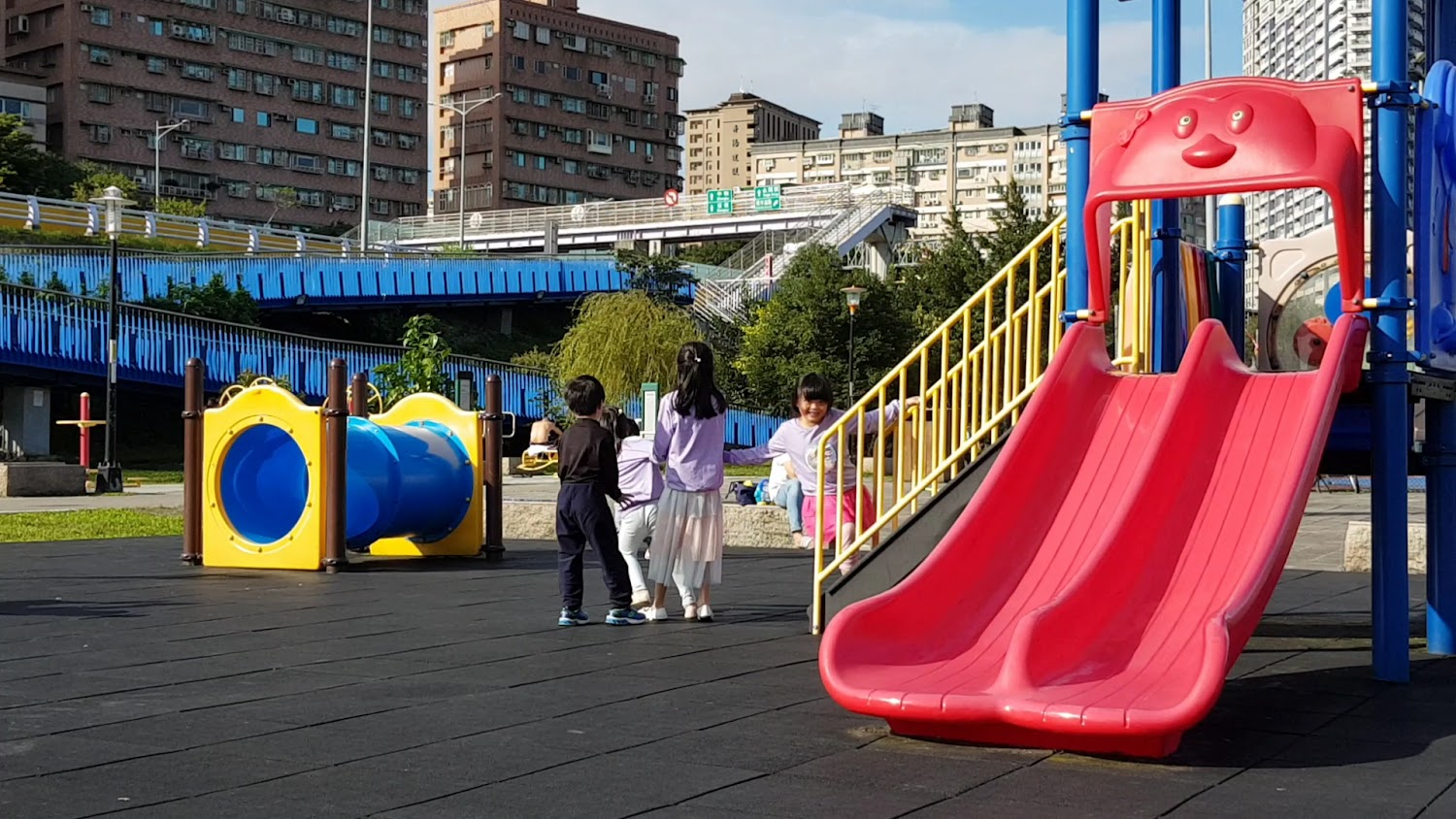 都市公園兒童遊樂場，有紅色雙滑梯與藍色通道隧道