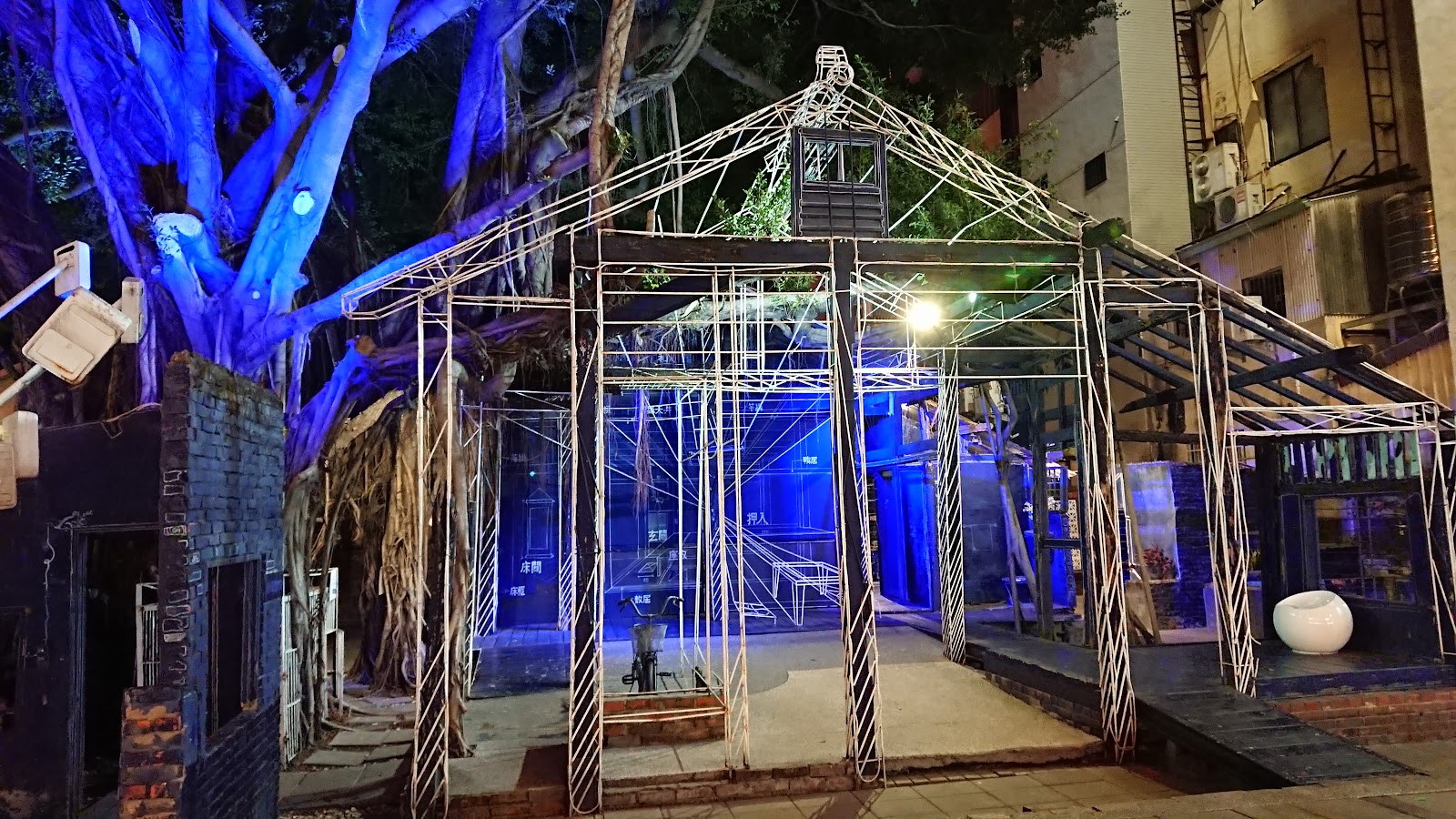 藍晒圖文創園區夜間鐵架裝置藝術，藍色光芒照亮老榕樹