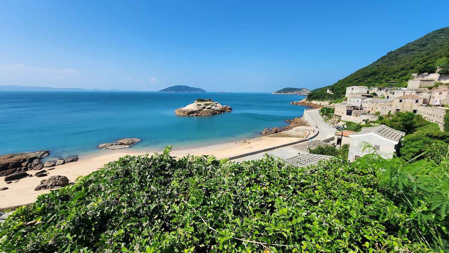 蔚藍大海沙灘岩石與依山而建的石頭房屋景色
