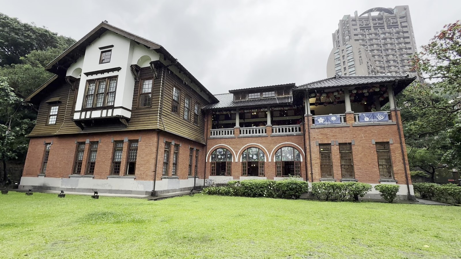 北投溫泉博物館建築側面陰天，紅磚底座深色木造上層，廊道掛藍色布旗