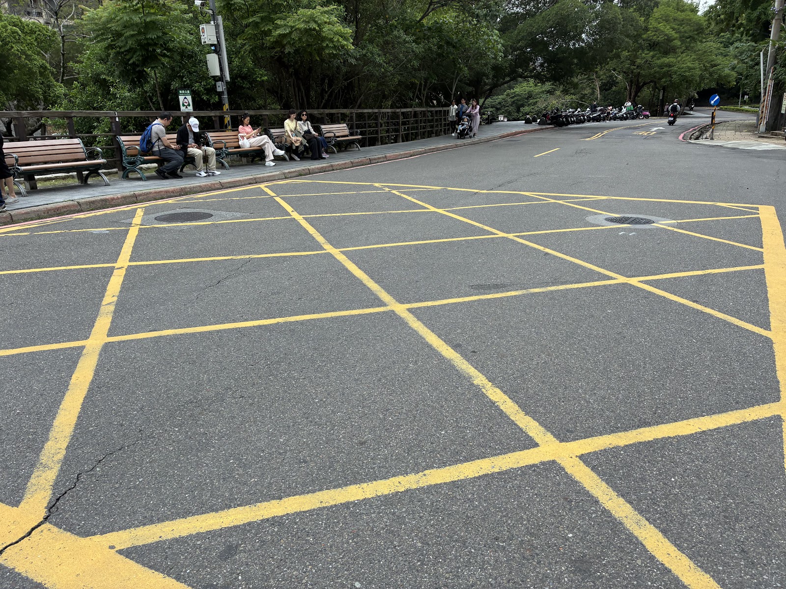 北投公園入口廣場，遊客坐在長椅休憩，背景綠蔭茂密