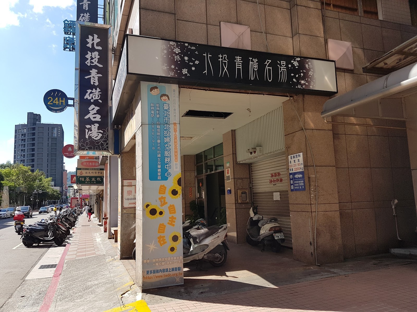 北投青磺名湯外觀招牌，24小時標誌清晰可見，日間晴天街道景象