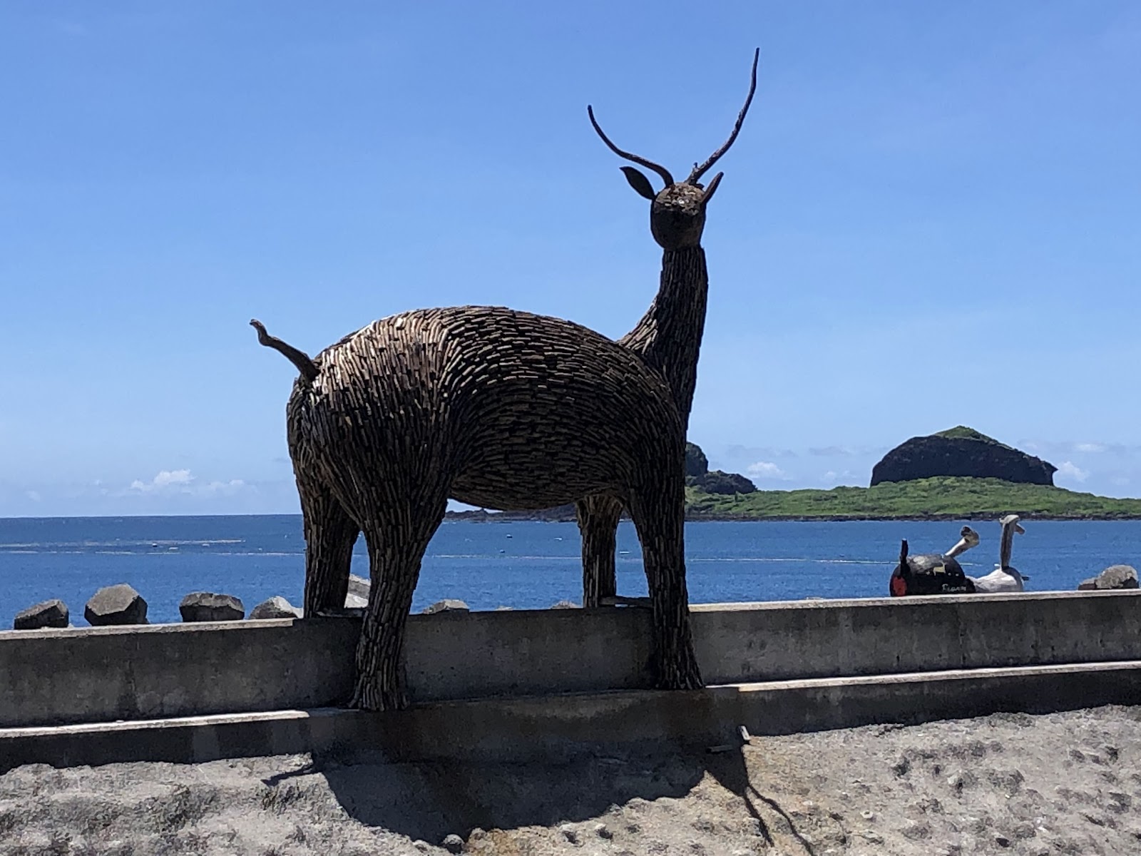 比西里岸部落石板拼貼梅花鹿雕塑，背景太平洋與三仙台島嶼，阿美族文化地標