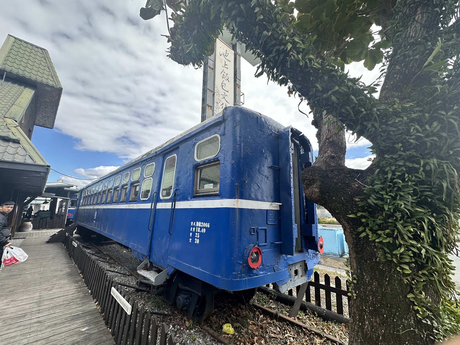 悟饕池上飯包文化故事館旁的藍色台鐵舊車廂特寫，車廂旁樹木茂密，旁邊有池上飯包文化指示牌