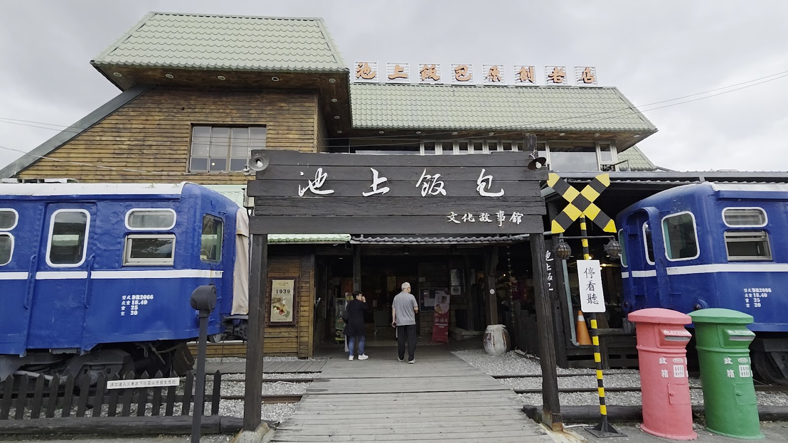悟饕池上飯包文化故事館全景，兩節藍色台鐵舊車廂停在館舍兩側，建築上方寫有池上飯包原創老店