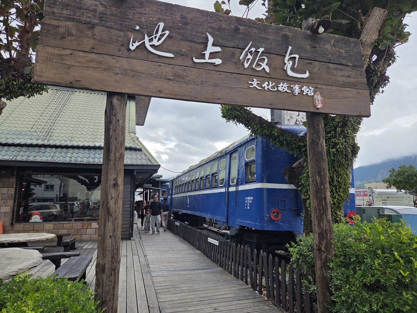 悟饕池上飯包文化故事館木製牌坊入口，牌匾寫著池上飯包文化故事館，後方藍色火車廂清晰可見