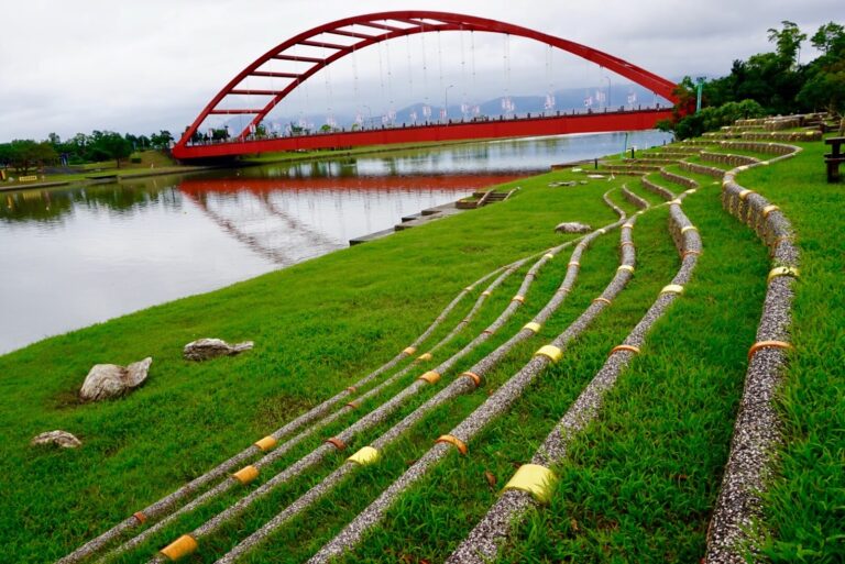 宜蘭冬山河親水公園紅色拱橋，彩虹橋倒映冬山河水面，前景竹籬笆裝置，翠綠草地