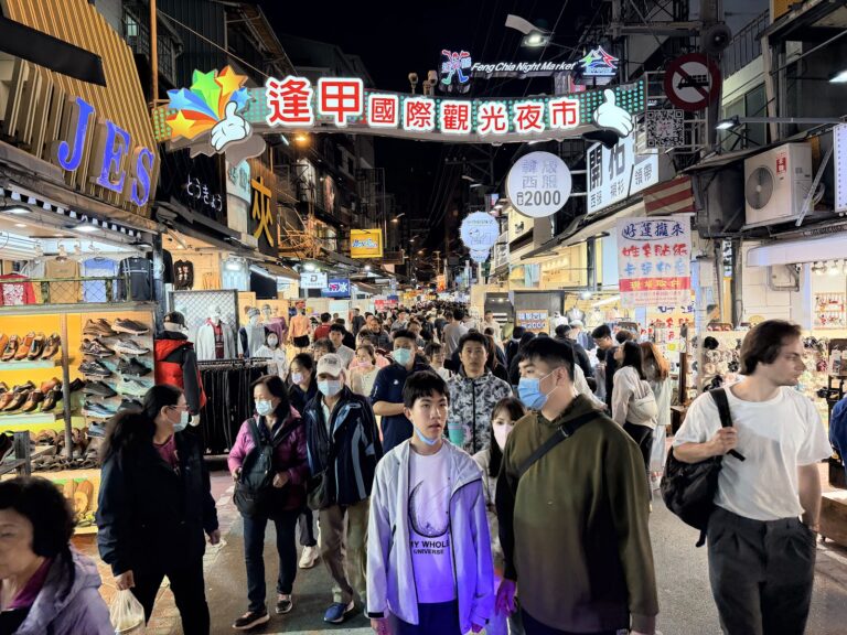 逢甲夜市主入口牌樓夜景，人潮熙攘，霓虹燈光閃爍，台中必訪夜市