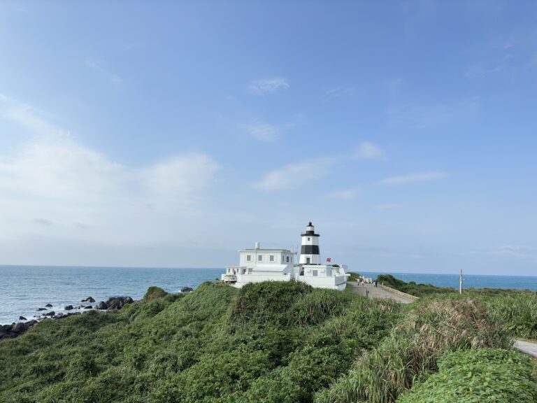 富貴角燈塔全景，台灣最北點，黑白相間燈塔矗立綠色山丘，台灣海峽碧海藍天