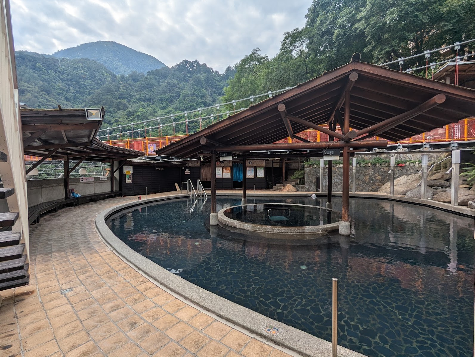 谷關溫泉飯店戶外弧形溫泉大池，木製涼棚遮蓋，背景青山