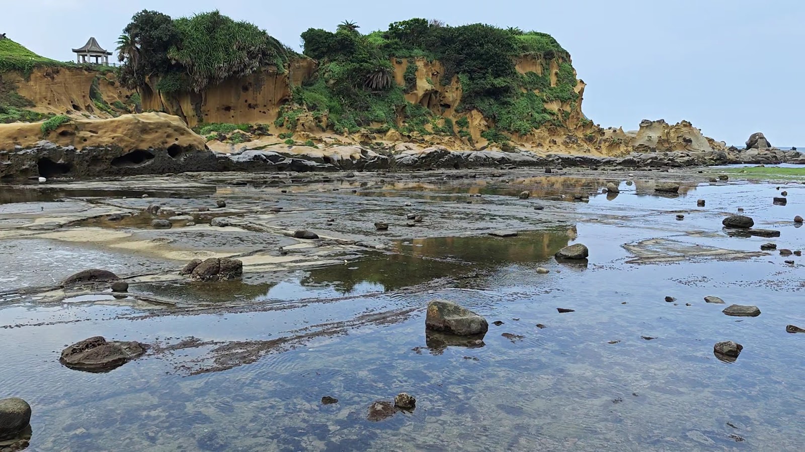 和平島海蝕岩盤潮間帶,退潮後形成透明積水淺灘,背景黃褐海蝕崖壁