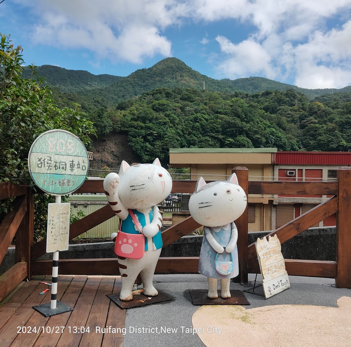 猴硐貓村入口貓咪公仔與猴硐車站牌，背景翠綠山丘藍天白雲