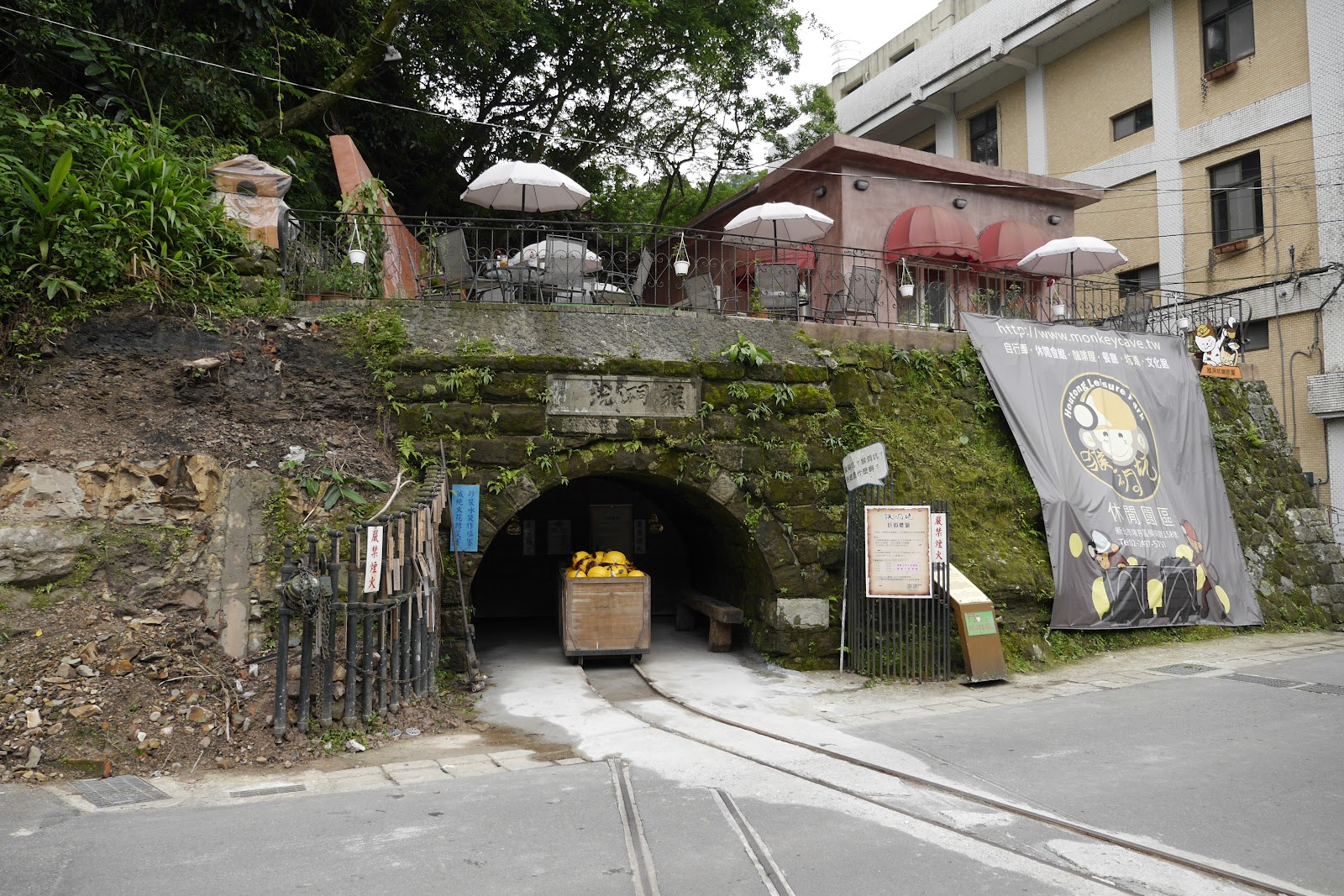 猴硐坑休閒園區石砌拱形礦坑入口，橘黃礦車停在軌道上