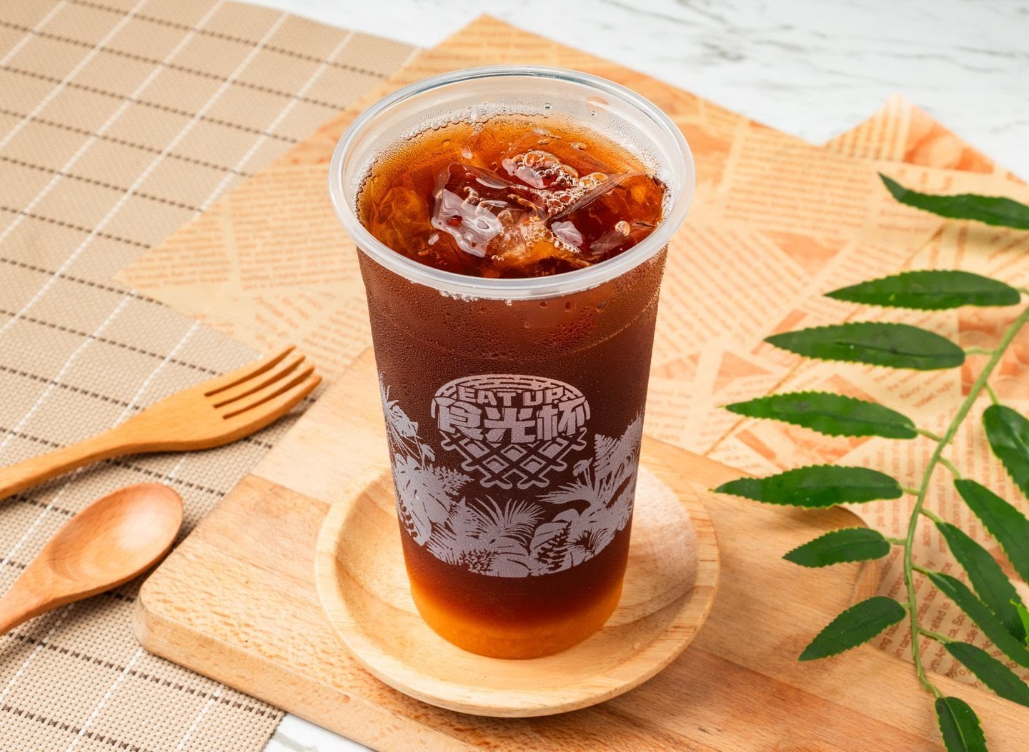 裝有冰塊的冷飲放在木托盤上，旁邊有木質餐具與植物葉子