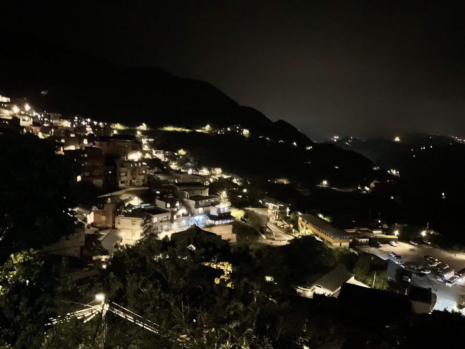 九份山城夜間全景，燈火隨山勢蜿蜒，遠山環抱