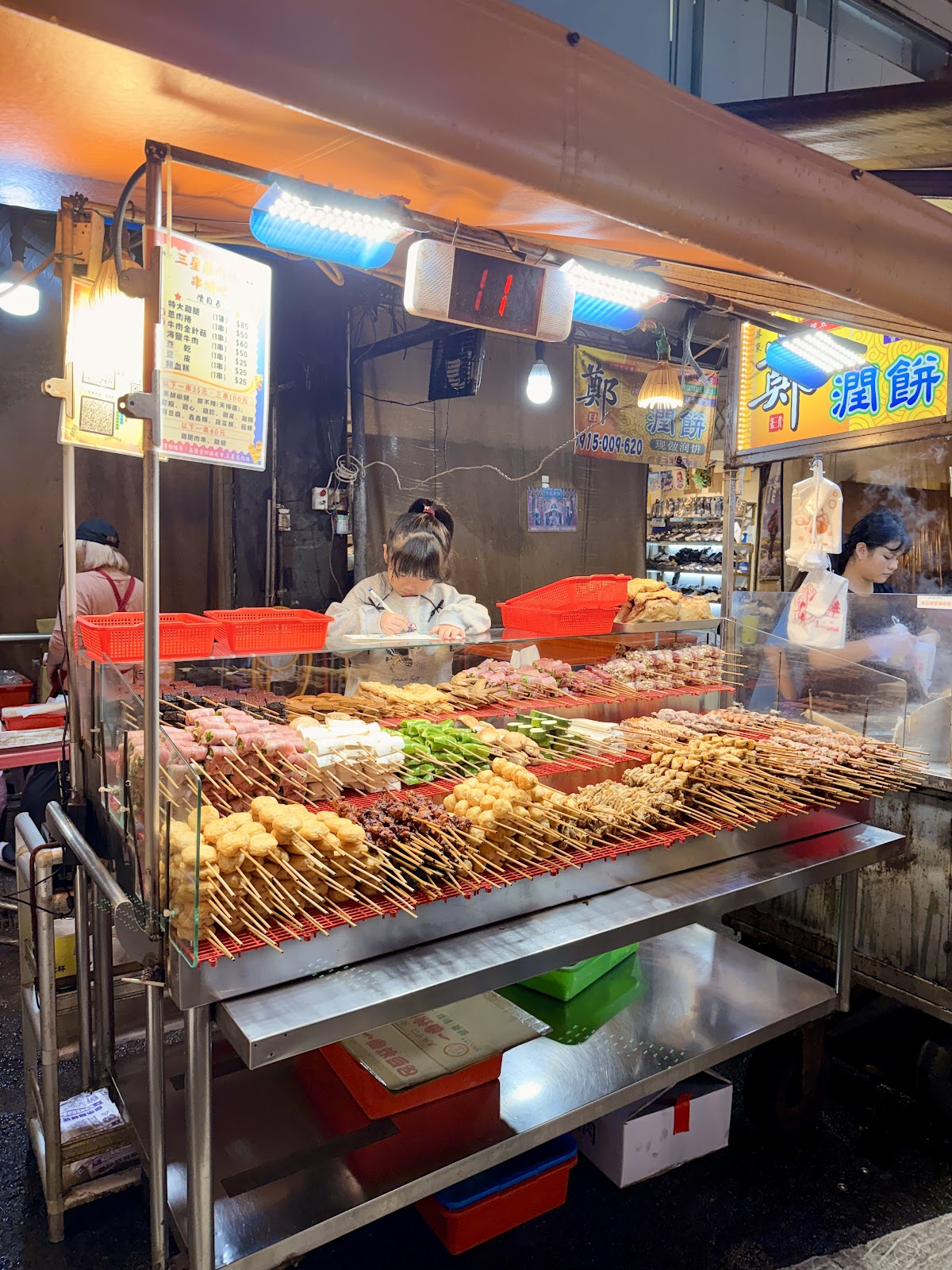 廟口夜市炸串烤串攤位，大量食物排列整齊，紅色碗盤
