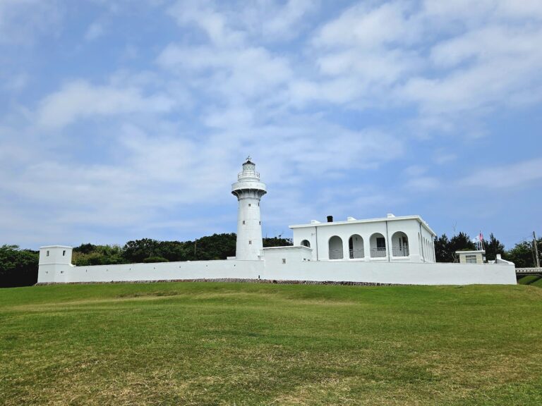 鵝鑾鼻燈塔全景，白色堡壘式建築矗立大草坪，墾丁旅遊必訪