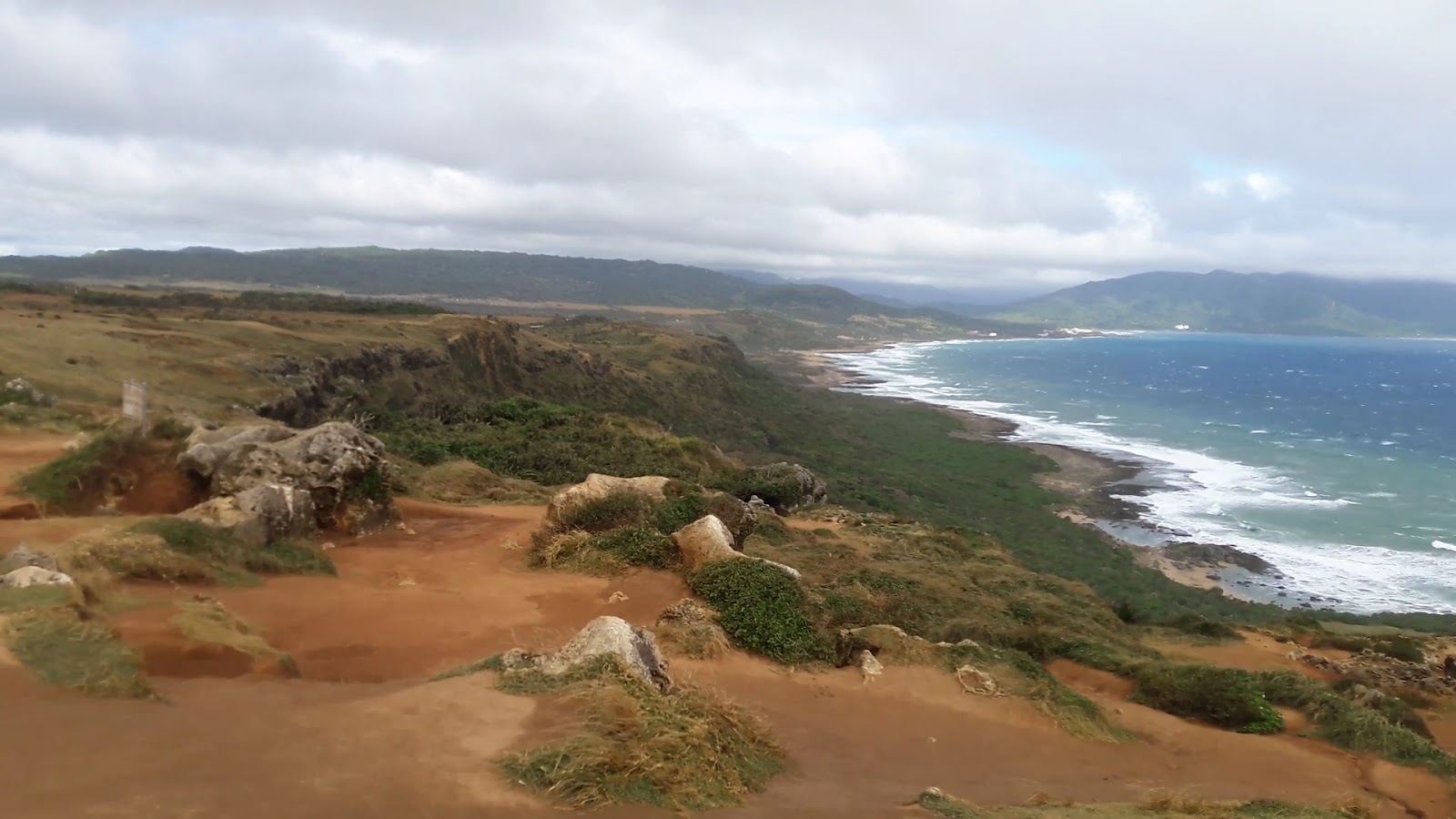 墾丁國家公園高地俯瞰,紅土礫石前景,翠綠矮叢,海浪沿礁岸延伸