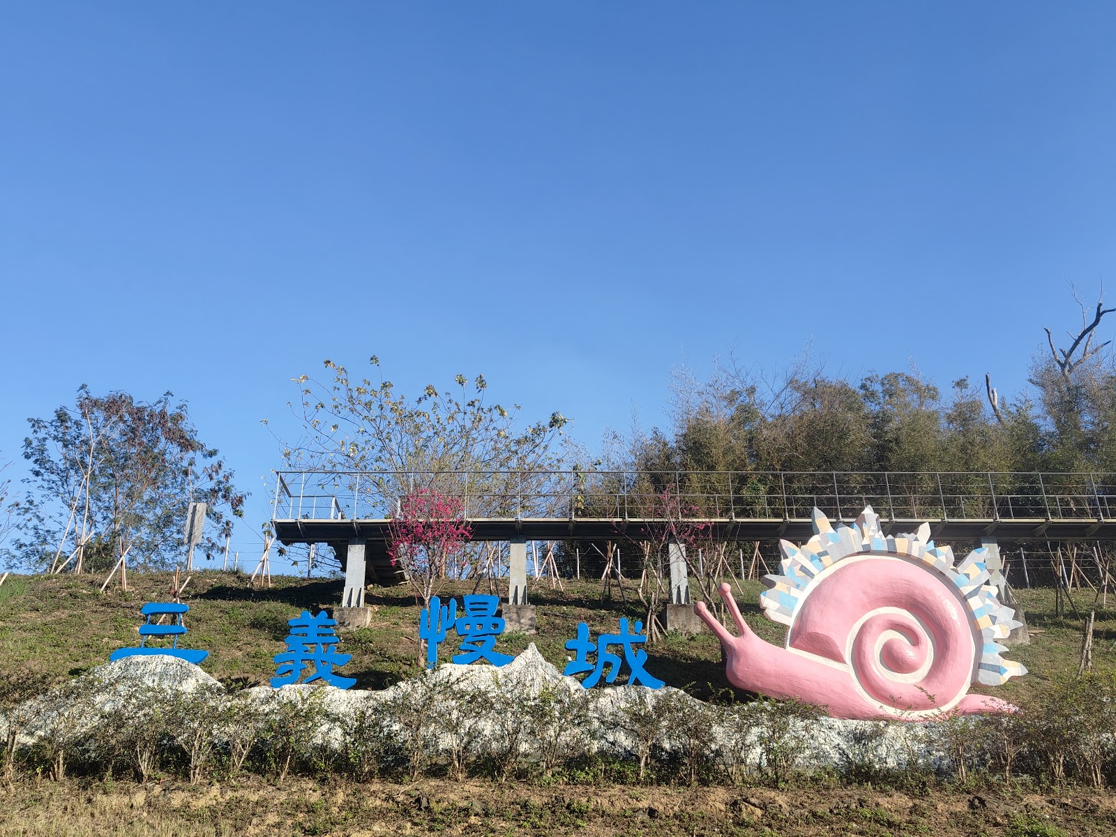 三義慢城景觀裝置，藍色大字招牌搭配粉紅色蝸牛雕塑