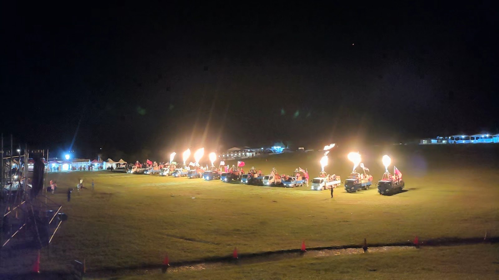 夜間草地火焰表演，多台貨車排列噴出火柱，嘉年華氛圍震撼