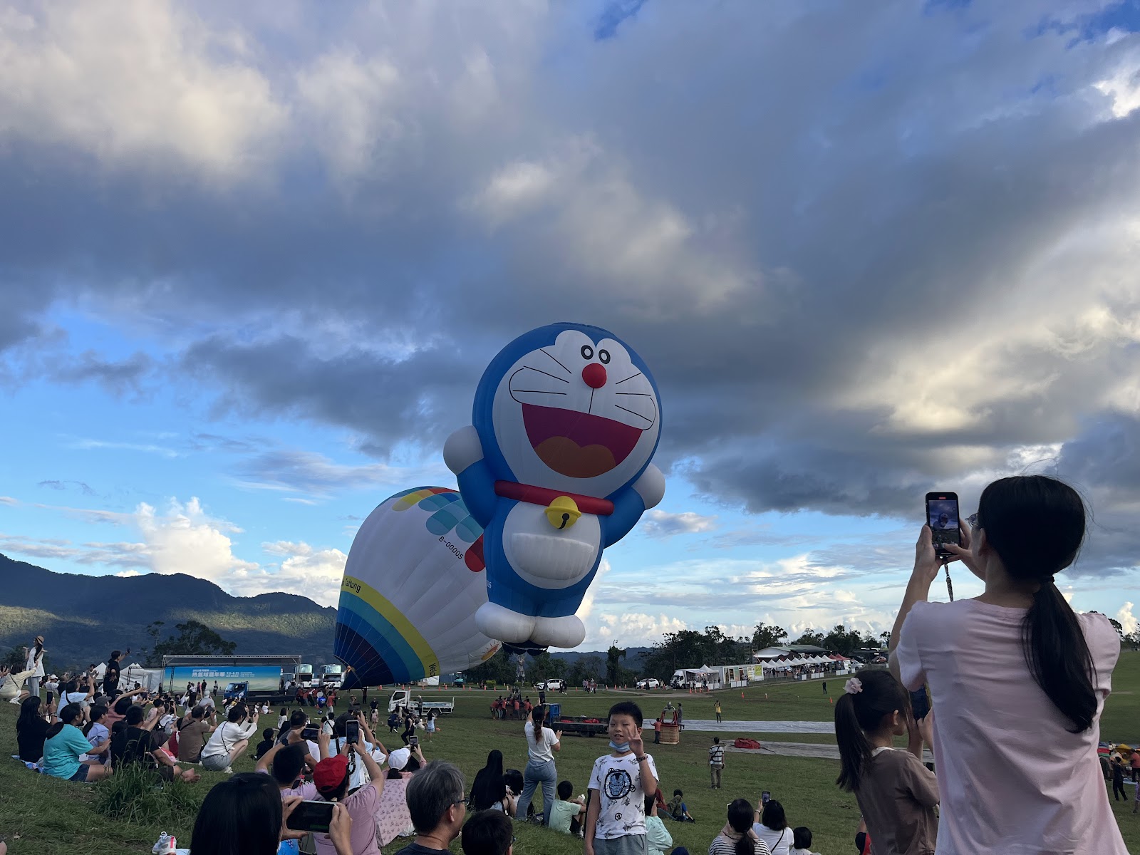 哆啦A夢造型熱氣球正面近拍，前景是觀眾席舉起手機拍照