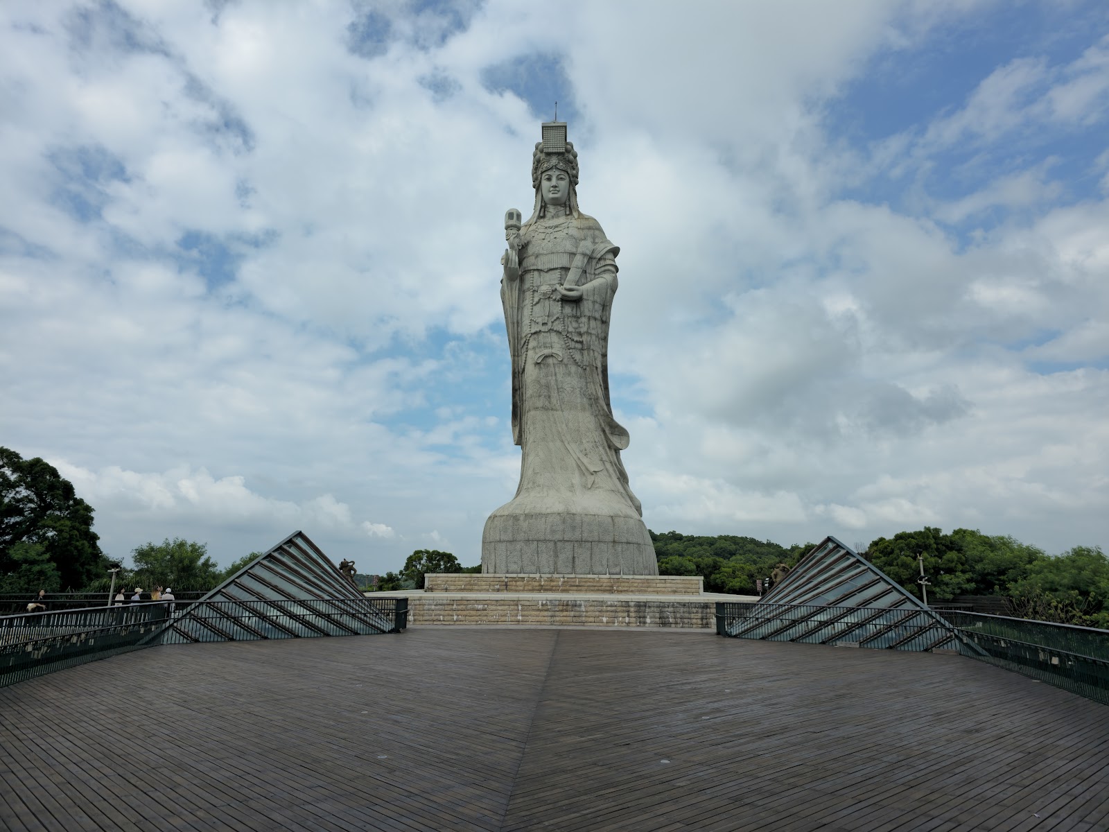 媽祖巨神像正面全景，白色神像高聳入雲，前方木製觀景平台，藍天白雲