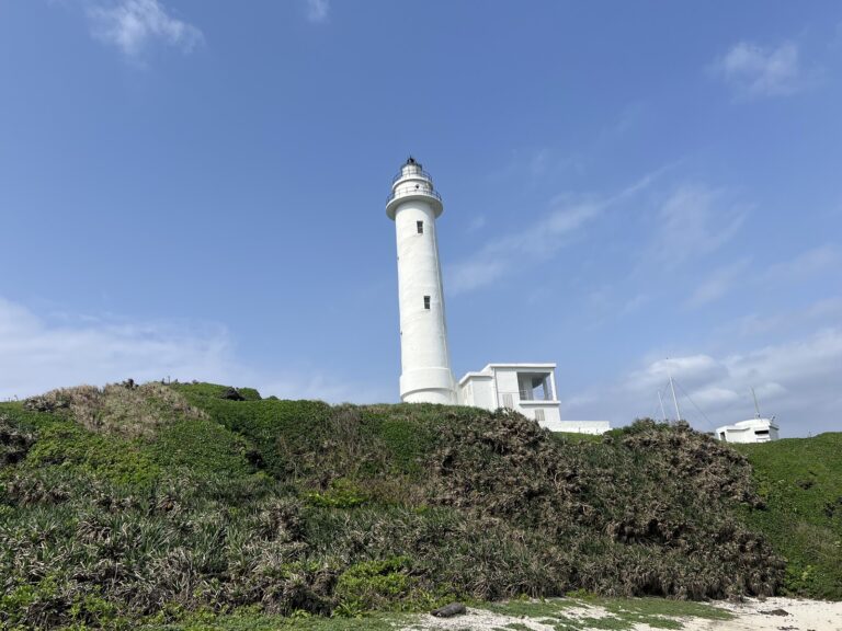 綠島燈塔白色塔身矗立藍天，前景綠意盎然