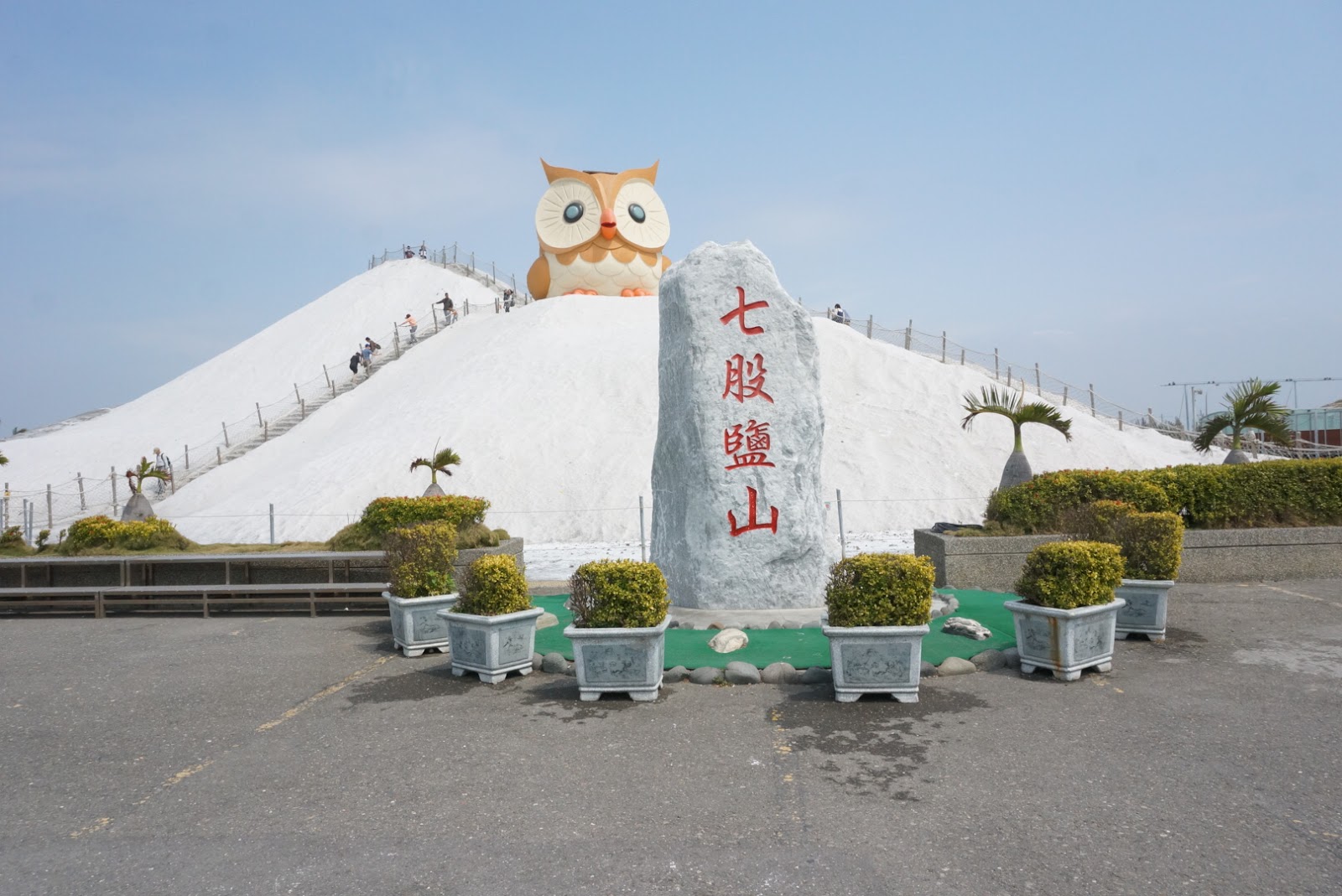 七股鹽山貓頭鷹吉祥物與七股鹽山石碑，盆栽環繞，遊客攀爬