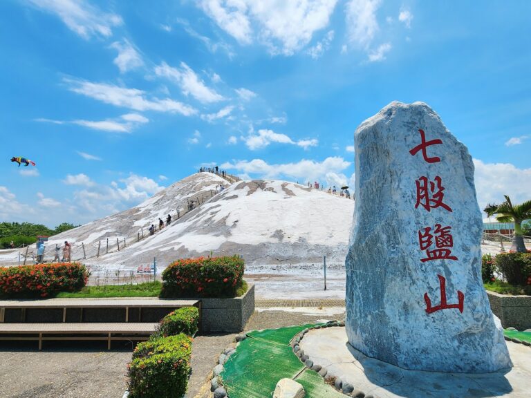 台南七股鹽山石碑側拍,遊客攀爬白色鹽山,天空有風箏飄揚
