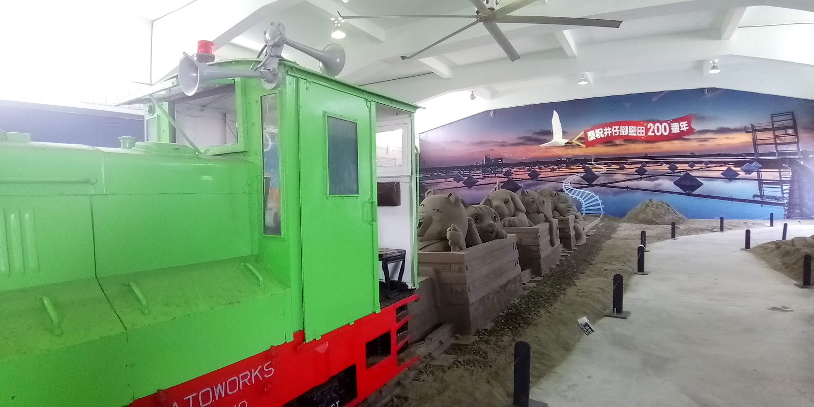 七股鹽山博物館室內，綠色復古小火車頭與沙雕牛群，鹽田200週年壁畫背景