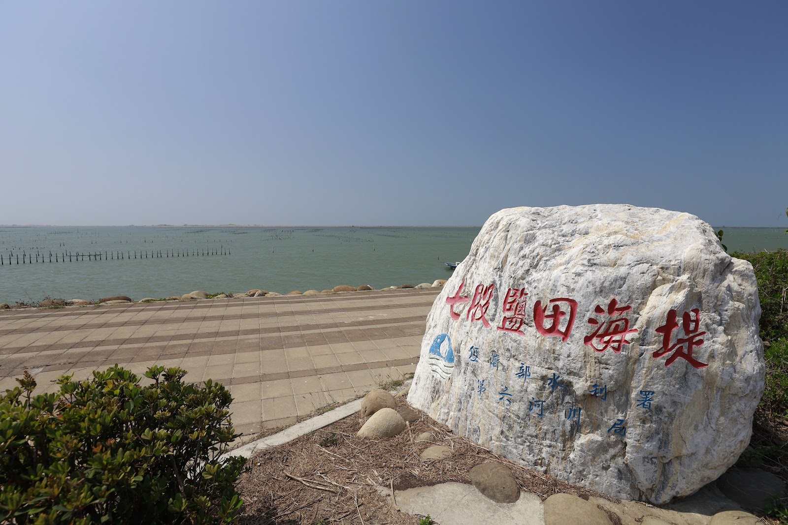 七股鹽田海堤石碑，背景台灣海峽海面與蚵架，晴天藍天