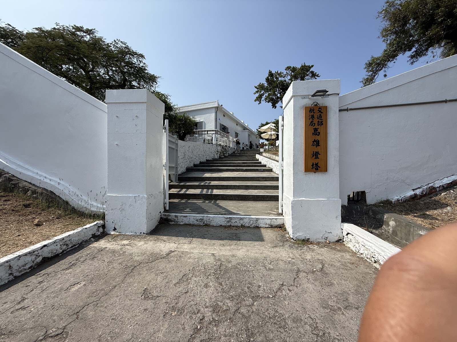 旗後燈塔入口石板步道，白色石柱大門立有高雄燈塔木製牌匾