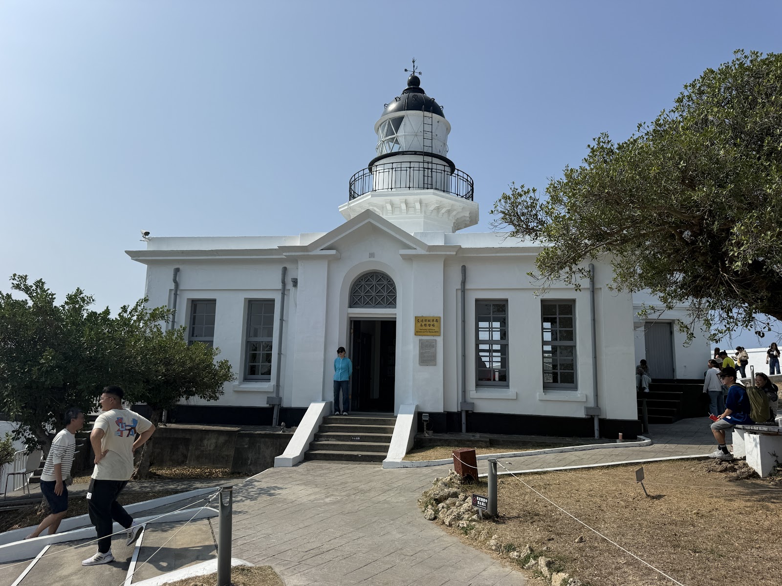 高雄旗後燈塔白色建築正面，歐式拱形門廊，藍天晴空，遊客參觀中