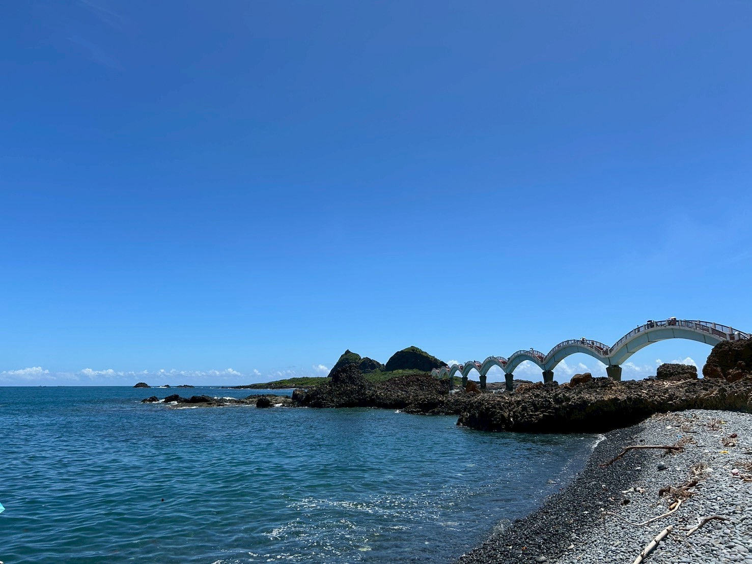 台東三仙台礫石海灘遠眺，白色橋拱與綠色島嶼在湛藍晴空下清晰可見
