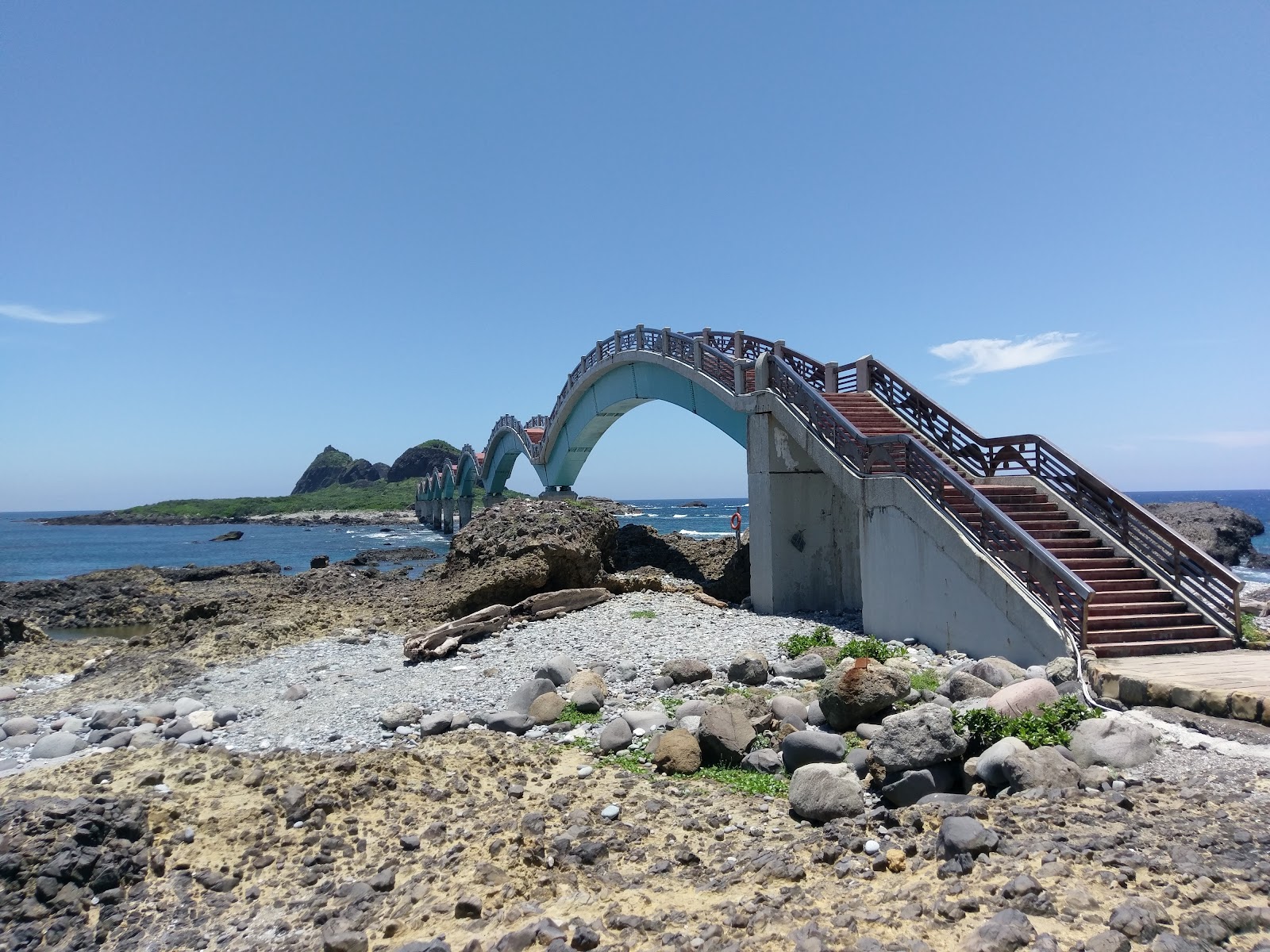晴天三仙台步橋全景，藍色橋拱清晰可見，礫石灘前景，三仙台島嶼在藍天下