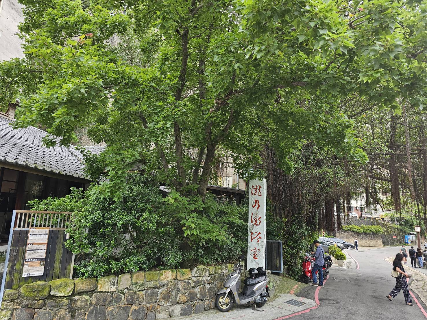 瀧乃湯浴室入口石柱門牌，傳統日式瓦屋頂建築被茂密綠樹環繞