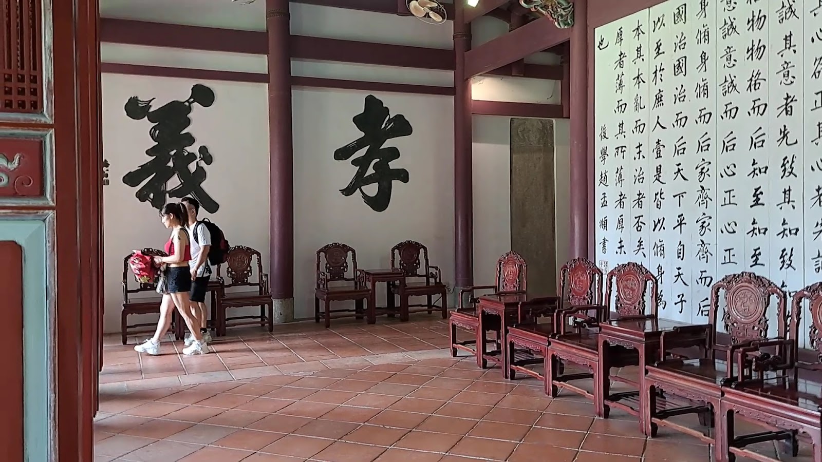 台南孔廟大廳內部，木椅環列，白牆書孝義大字，遊客穿行而過