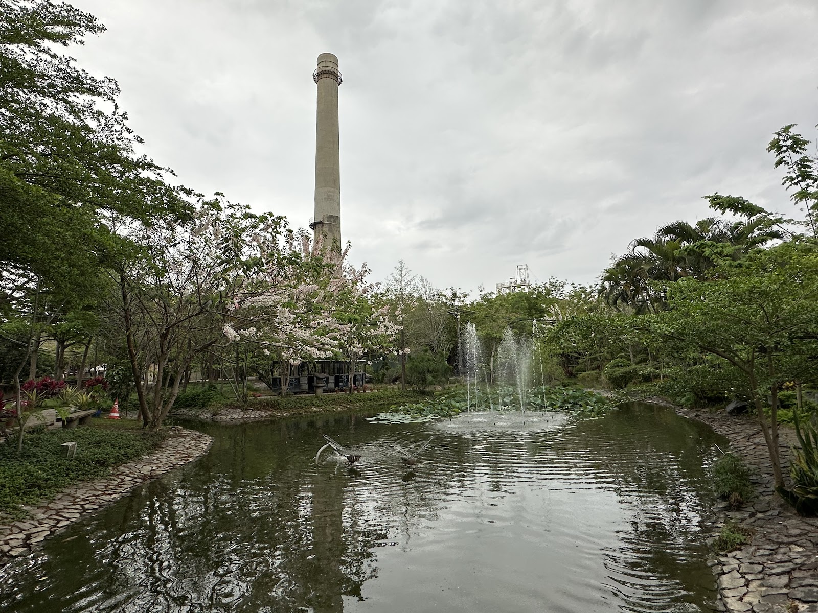 台南十鼓仁糖文創園區戶外噴水池,背景為糖廠特色煙囪與粉色花叢綠樹