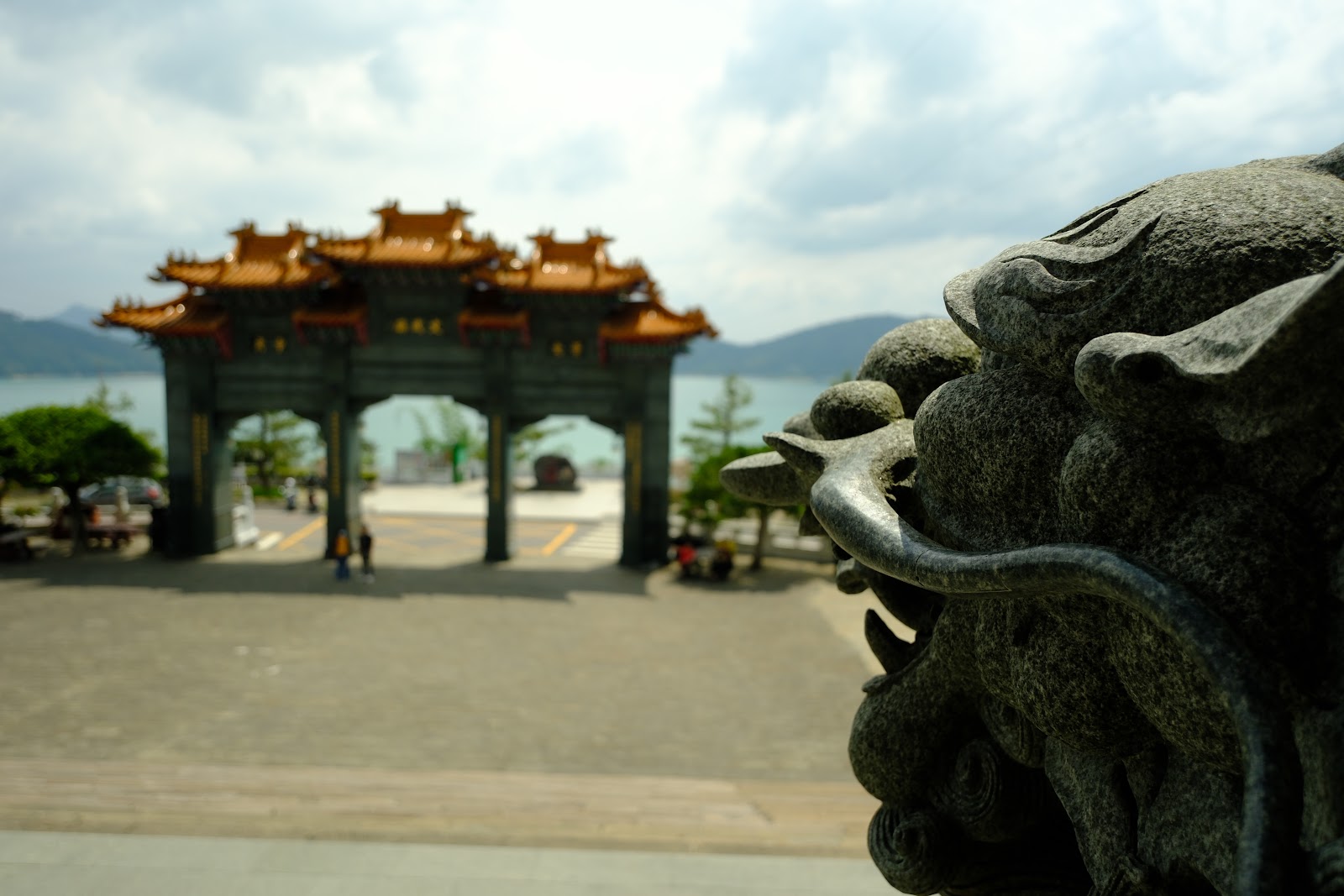 文武廟入口牌坊，前景深色石獅近拍，背景金黃廟頂牌樓