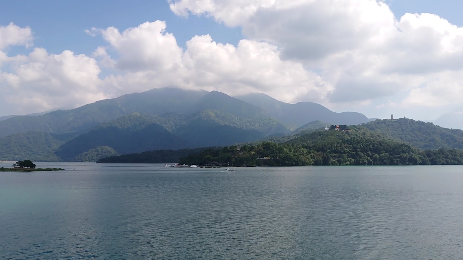 向山觀景台望向對岸，翠綠山丘上廟宇隱現，湖面快艇劃過
