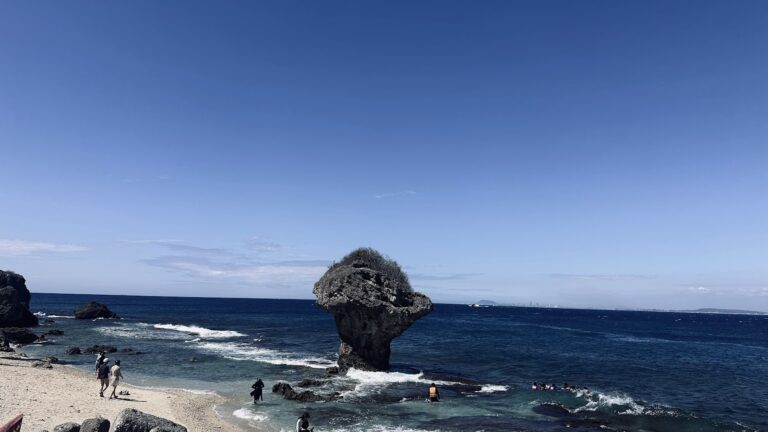小琉球花瓶石全景，晴天湛藍大海，遊客在沙灘漫步和浮潛