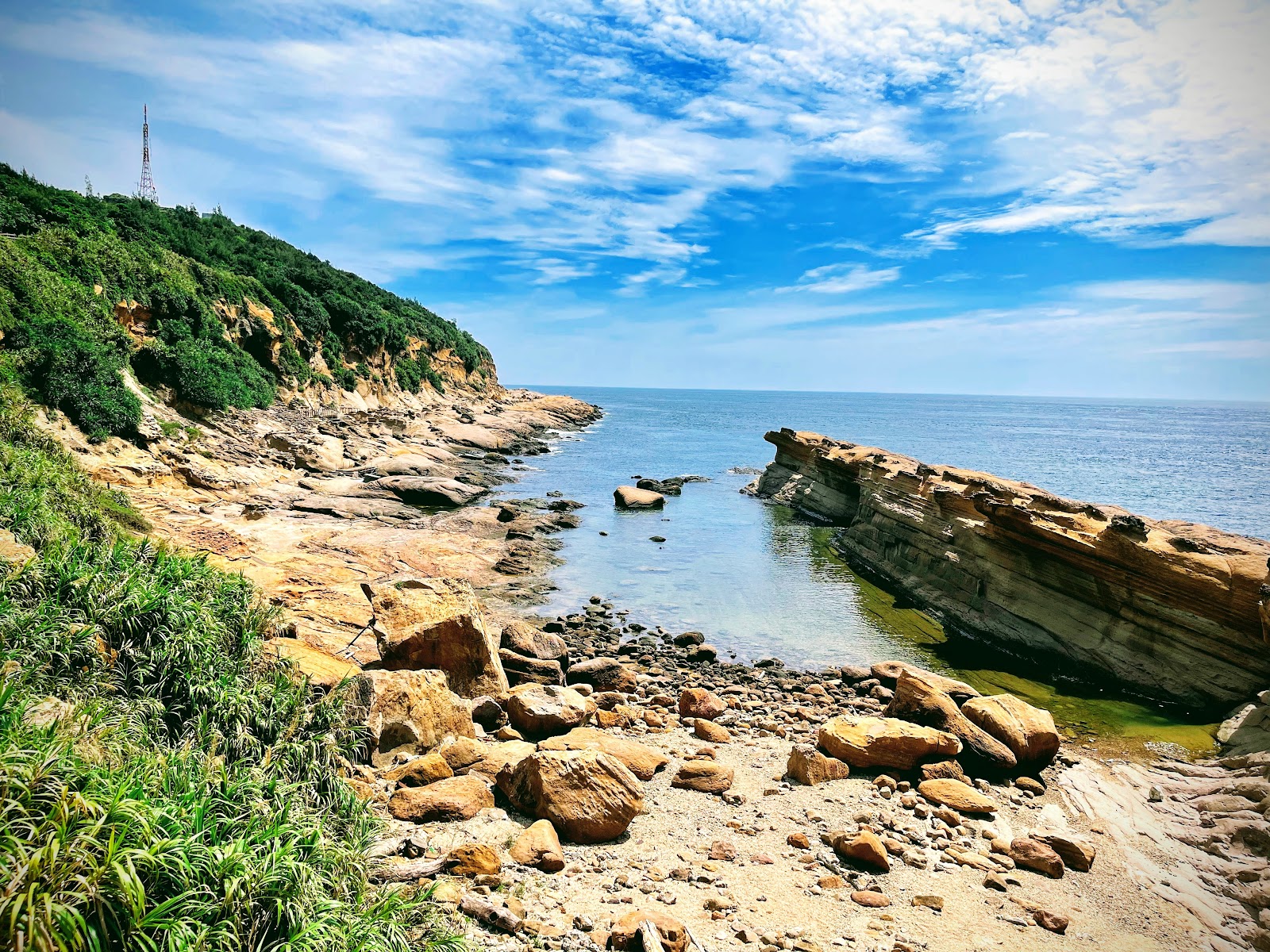 野柳北海岸全景,傾斜層狀礁岩伸入碧藍海中,前景礫石灘,藍天白雲