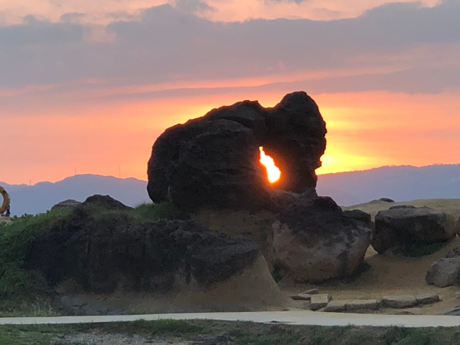 野柳蕈狀岩夕陽剪影,橙紅餘暉從岩洞透射而出,黑色岩石剪影與橙紅天空