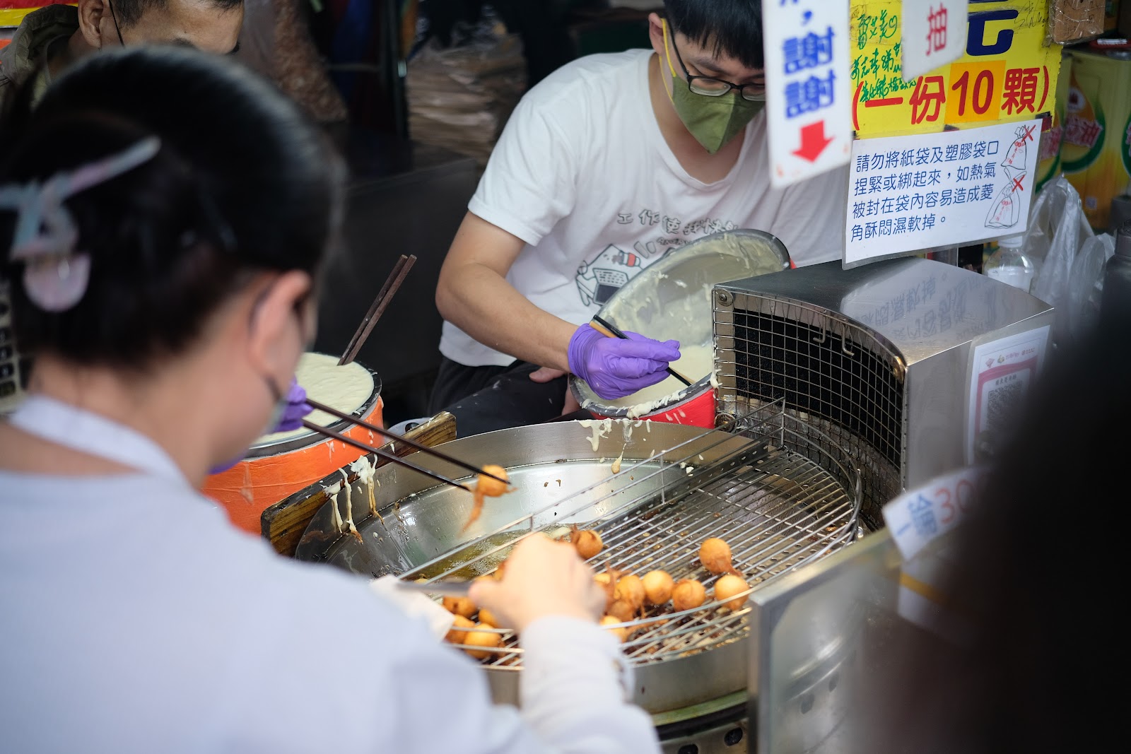菱角酥現炸鍋特寫,員工戴紫手套翻炒,旁邊一份10顆說明牌